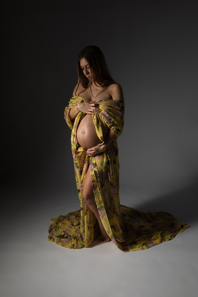 Photographie artistique de grossesse en studio, future maman enveloppée dans un tissu jaune floral – séance maternité haut de gamme à Paris, Bordeaux et Aix-en-Provence.