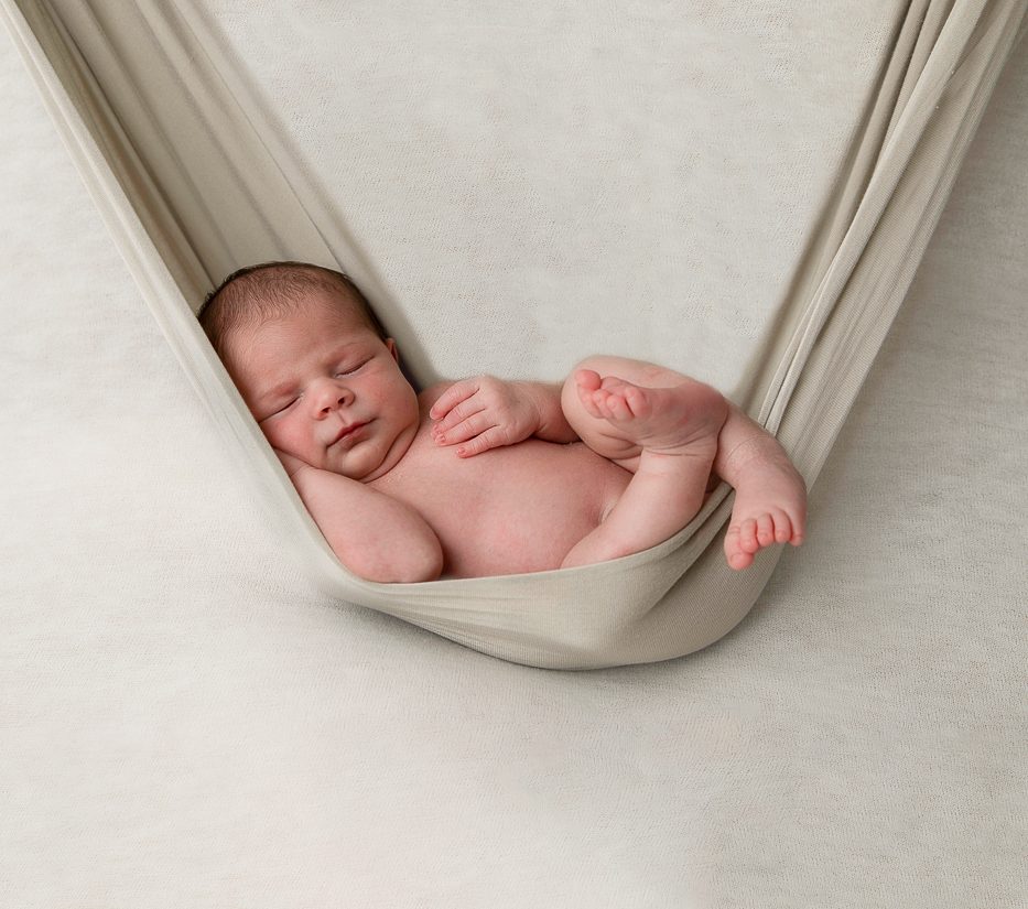 Photographie artistique de nouveau-né endormi, emmailloté dans une couverture douce – séance photo naissance haut de gamme à Paris, Bordeaux et Aix-en-Provence.